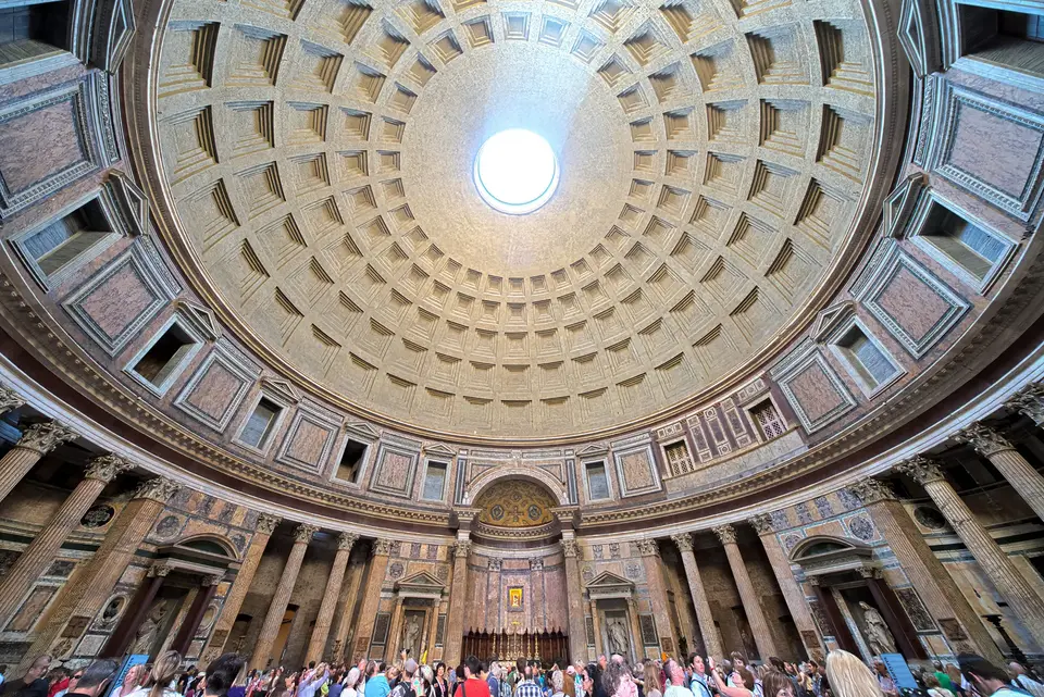 Sunlight beams through oculus above throngs of tourists.